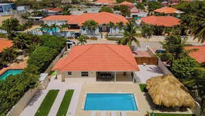 Un quartier résidentiel où les maisons se distinguent par leurs toits recouverts de tuiles rouges, une piscine et des palmiers.
