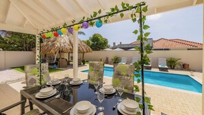 Un espace extérieur aménagé pour les repas, avec vue sur la piscine, des parasols en chaume et des chaises longues.