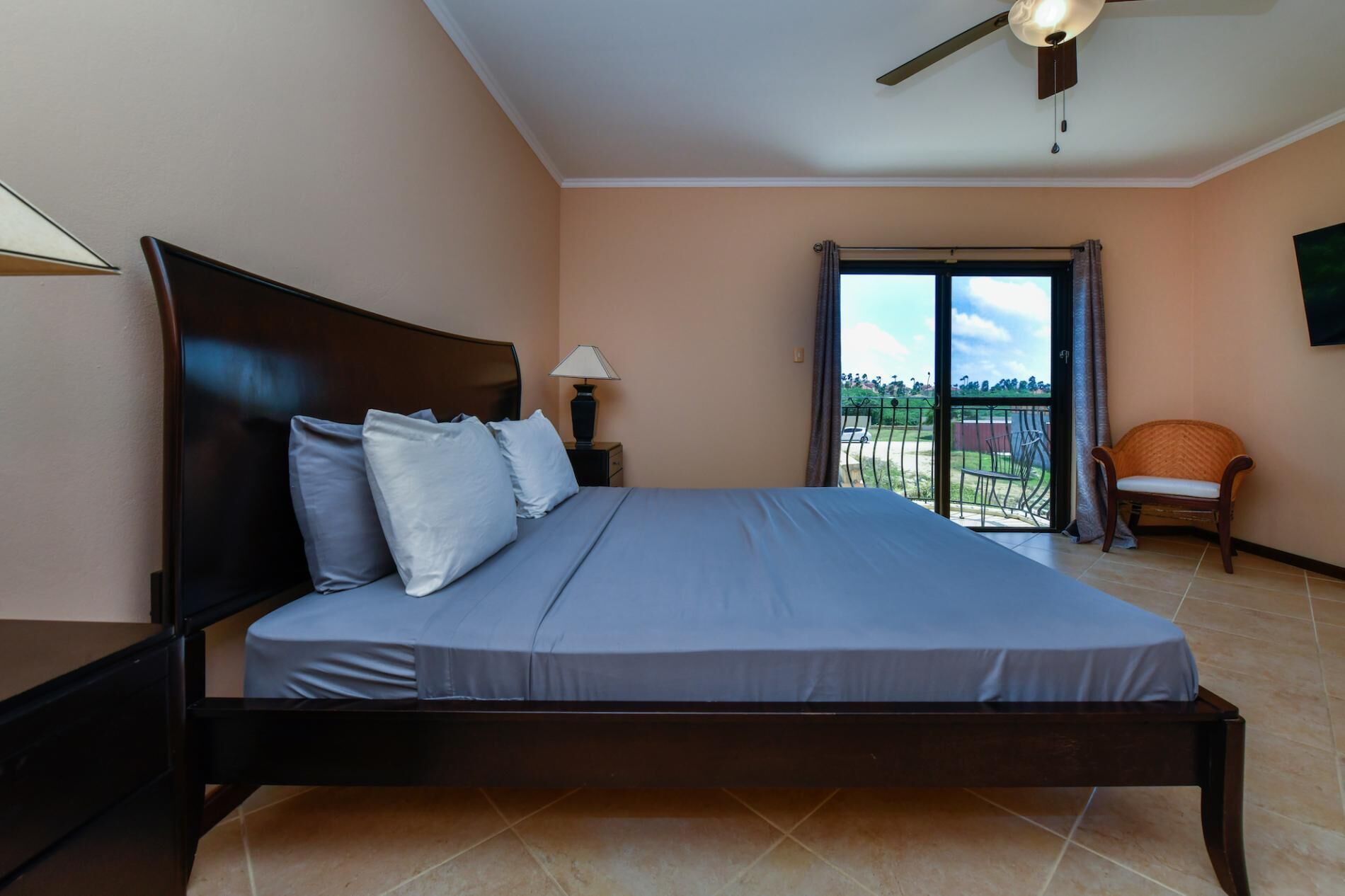 Un dormitorio con cama, mesita de noche, lámpara, silla y balcón con vistas.