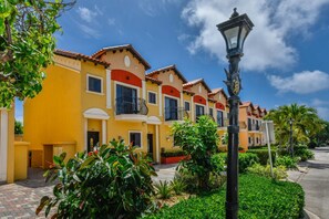 Una hilera de edificios amarillos con detalles en rojo y balcones, rodeados de vegetación y un farol.