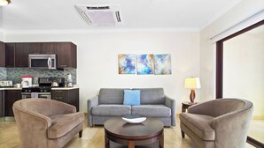 A modern living room with a grey sofa, two armchairs, a coffee table, and a kitchen in the background.