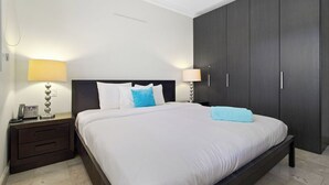 A modern hotel room with a large bed, dark wooden wardrobe, and bedside lamps.
