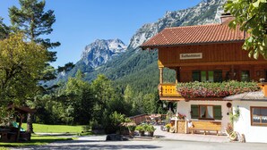 A wooden building with a balcony, surrounded by greenery and mountains. - 5-Star Vacation Rental in Wimbachtal, 45 sqm, Sleeps 2, Wi-Fi (Ramsau bei Berchtesgaden)