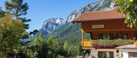 A wooden building with a balcony, surrounded by greenery and mountains.