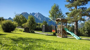 A playground with a slide and climbing area, surrounded by lush green grass and trees, with mountains in the background. - 5-Star Vacation Rental in Wimbachtal, 45 sqm, Sleeps 2, Wi-Fi (Ramsau bei Berchtesgaden)