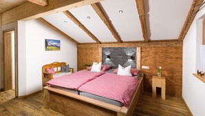 A bedroom with a wooden bed, checkered bedding, a stone wall, and a small bedside table with a vase. - 5-Star Vacation Rental in Wimbachtal, 45 sqm, Sleeps 2, Wi-Fi (Ramsau bei Berchtesgaden)