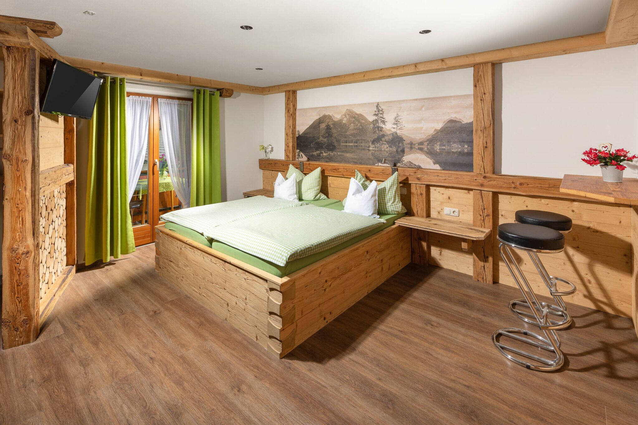 Quarto com estrutura de madeira, cama, televisão, janela com cortinas e um quadro na parede.