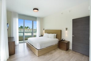 A modern hotel room with a large bed, a bedside table, a nightstand, a wardrobe, and a balcony with a view. - Ocean View Wraparound Balcony and Rooftop Pool-CS1 (Hollywood)