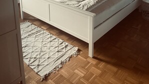Une chambre avec un plafond en bois, un lit blanc avec une literie à motifs, une table de chevet avec une lampe et un luminaire suspendu.