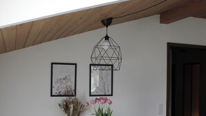 Un espace repas avec une table blanche, des chaises noires et un luminaire suspendu aux motifs géométriques.