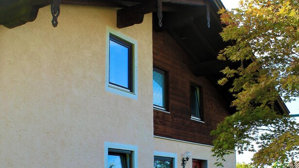 Un bâtiment à deux étages, à la façade beige, avec une porte rouge et un petit jardin délimité par une clôture en bois.