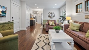 Ein geräumiges Wohnzimmer mit Holzböden, einem weißen Couchtisch, einem braunen Sofa und einem grünen Sessel.