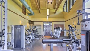 Un gimnasio con diversos equipos de ejercicio, incluyendo cintas de correr y máquinas de pesas, dispuesto en una sala amplia con vigas de madera en el techo.