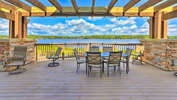 Terraza techada al aire libre con una mesa y sillas, con vista a un lago y follaje.