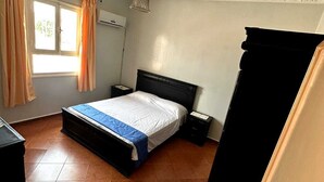 Un dormitorio con cama, mesitas de noche, armario, ventana con cortinas y lámpara en el techo.
