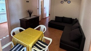 Una sala de estar con un sofá negro, una mesa amarilla con sillas a rayas, un mueble de madera oscura y un reloj de pared decorativo.