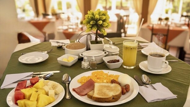 Uma mesa de café da manhã com torradas, ovos e frutas, além de uma xícara de café e um copo de suco.