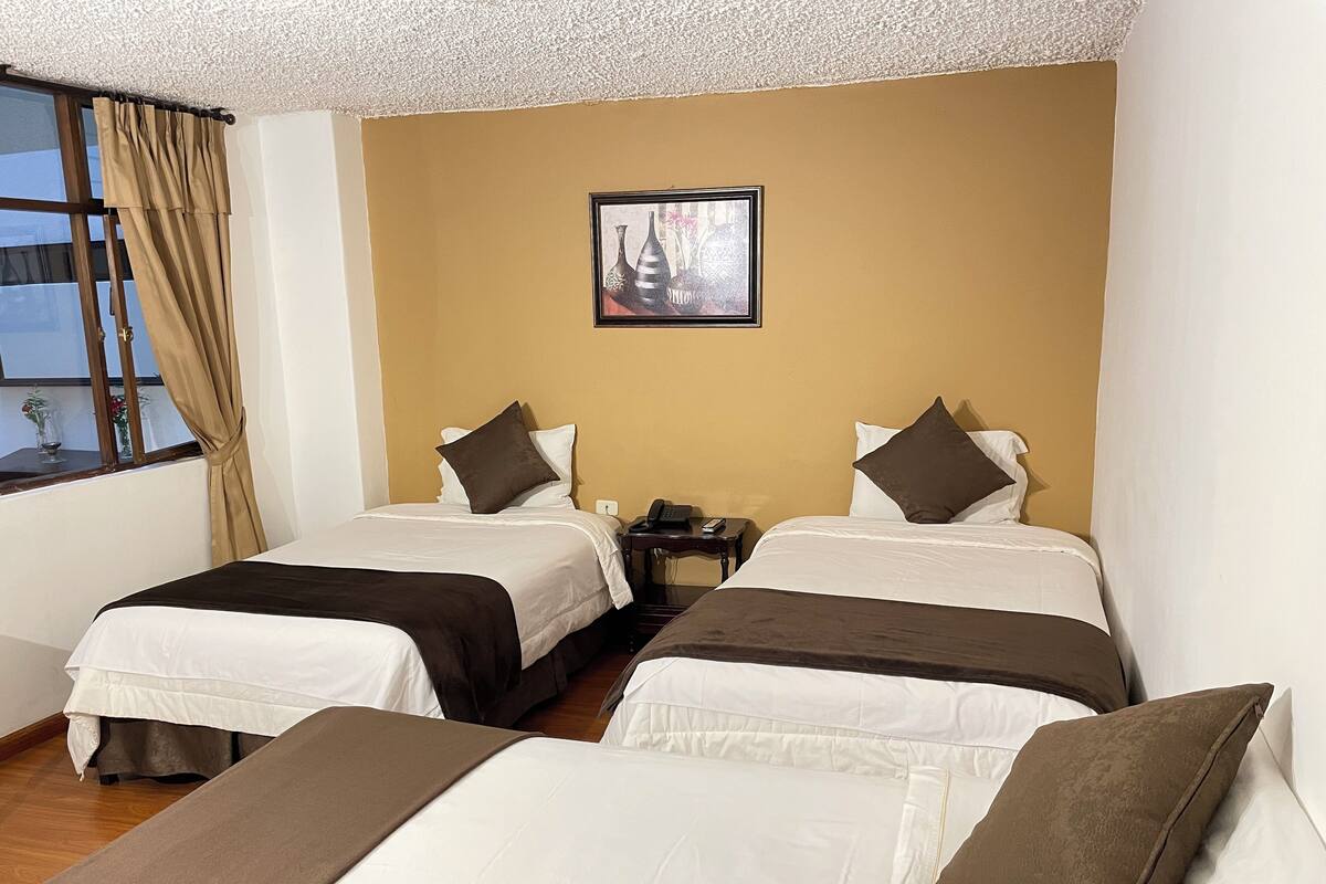 A hotel room with two beds, a nightstand with a phone, and a framed picture on the wall.