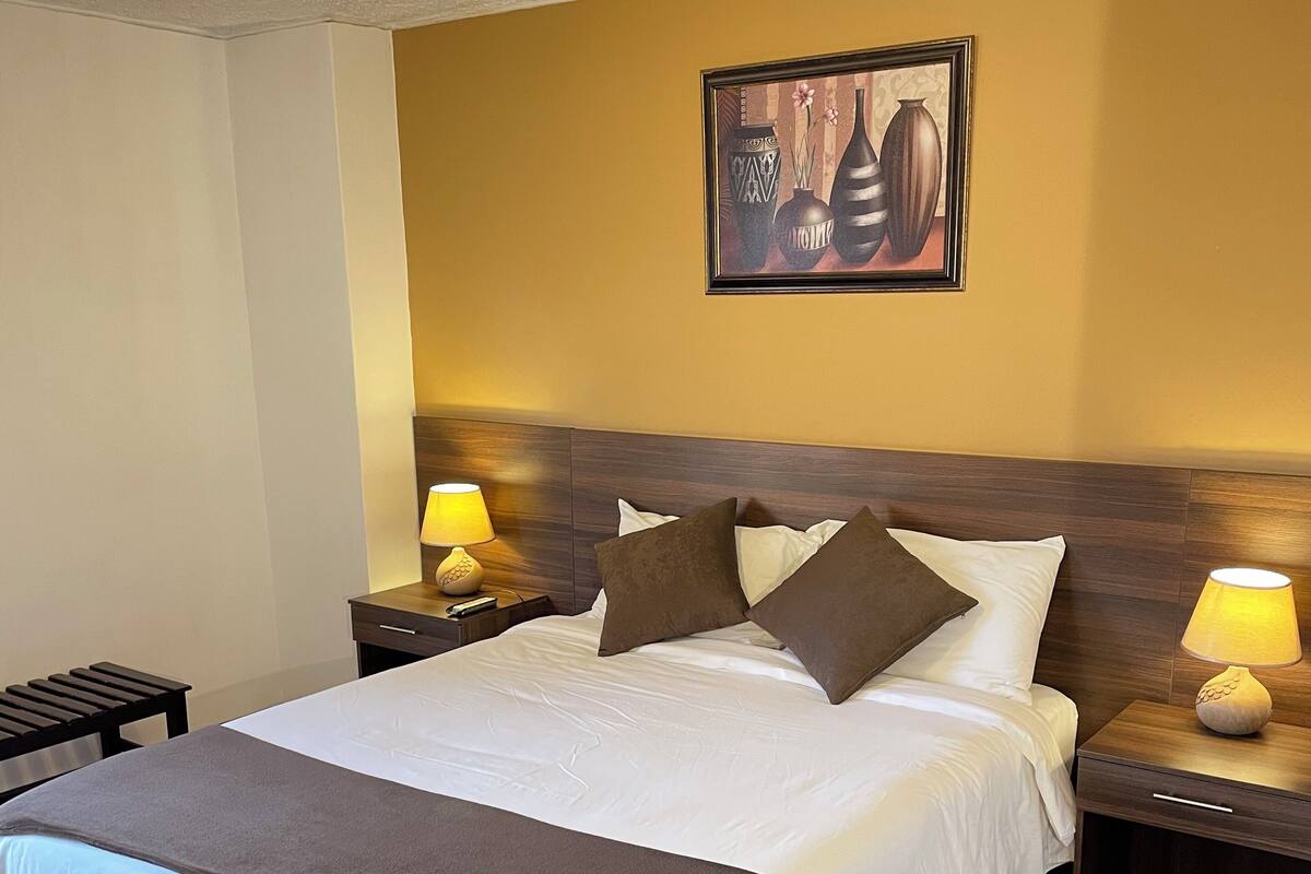 A neatly made bed with a brown throw, two bedside lamps, and a framed artwork on the wall.