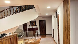 Um corredor amplo com piso de madeira, escada com corrimão de madeira e um balcão de recepção.