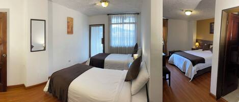 A hotel room with two beds, a wooden floor, a large window with curtains, and a ceiling light.