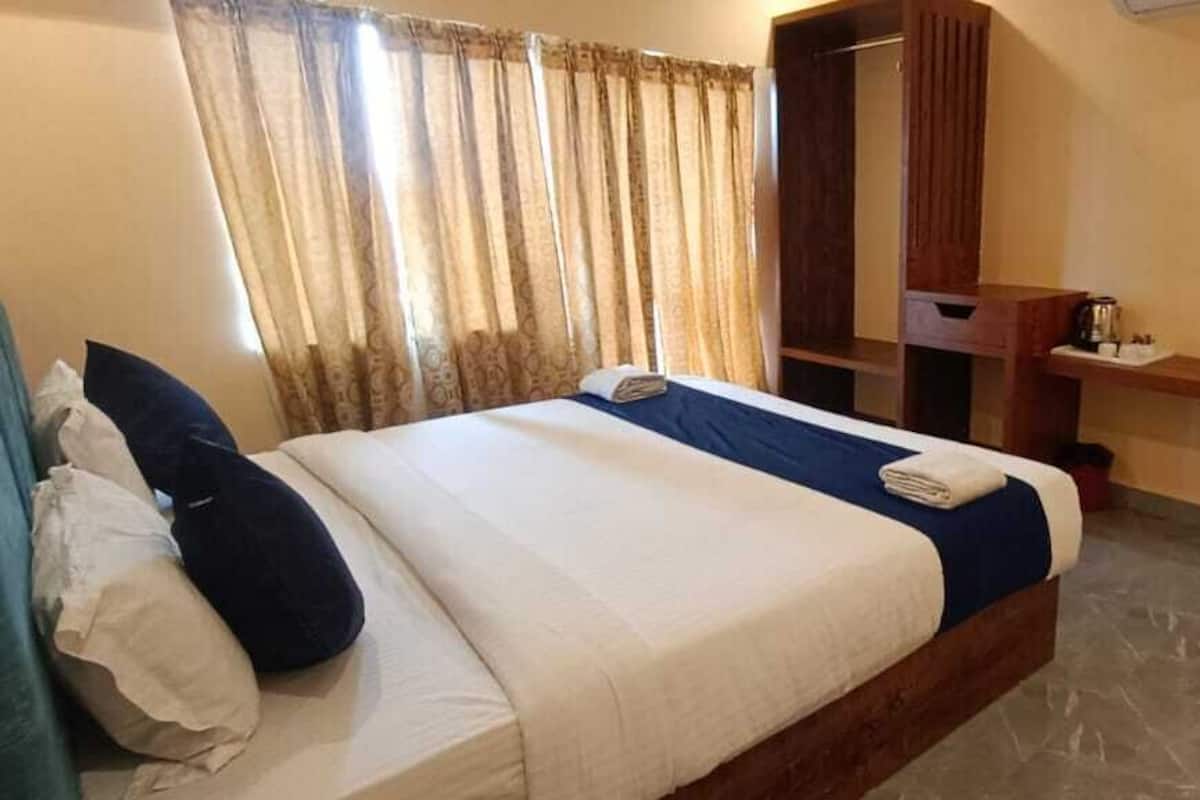 A hotel room with a bed, a wooden wardrobe, a small table with a cup, and a mirror.