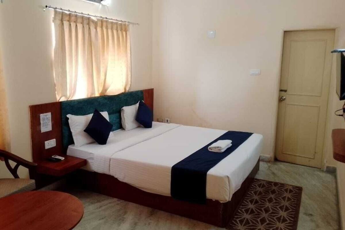 A hotel room with a bed, a desk, a chair, and a door.