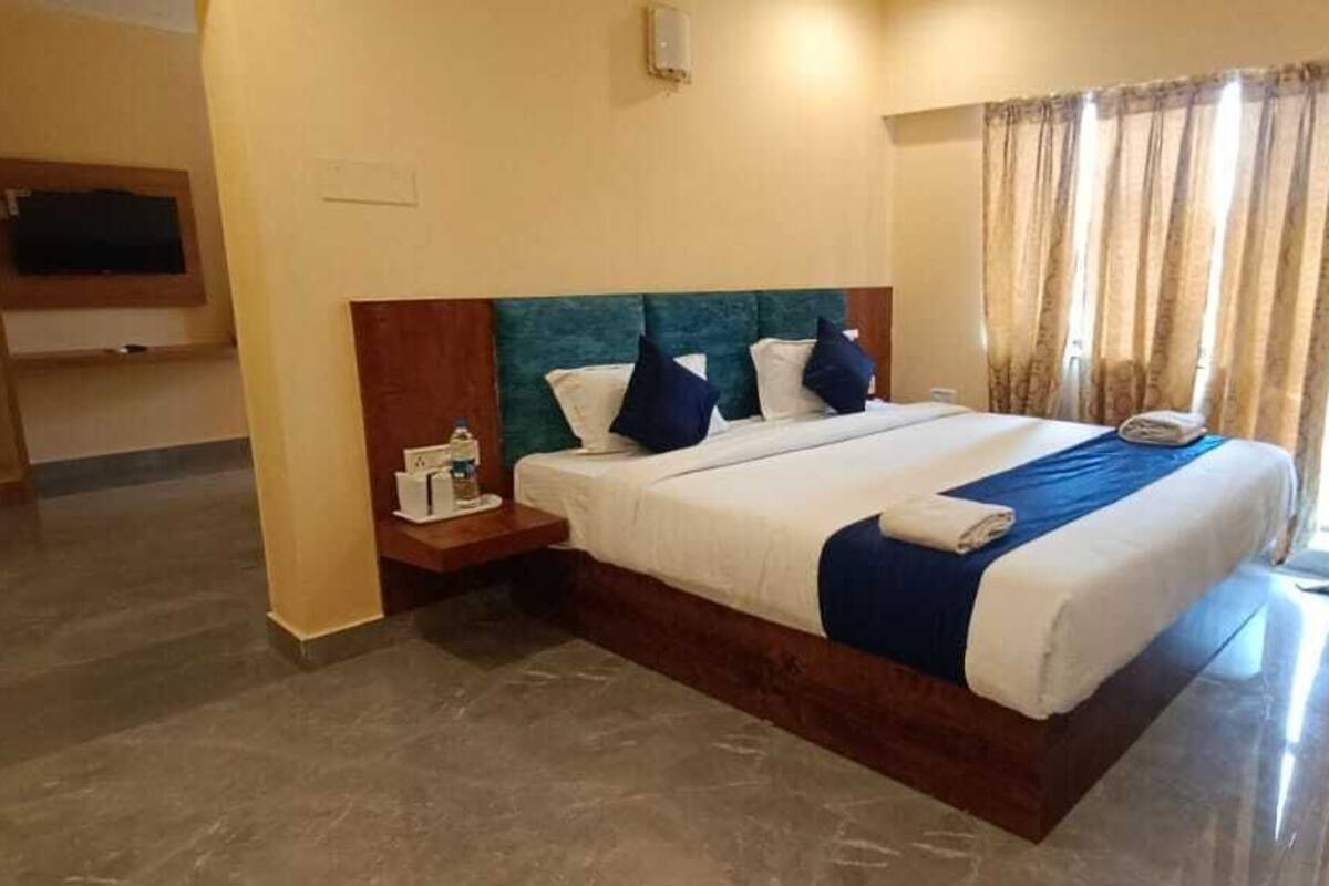 A hotel room with a large bed, a bedside table, a TV, and a window with curtains.