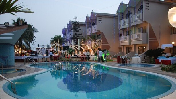 An outdoor swimming pool with multiple lanes, surrounded by buildings with balconies and string lights. - Hotel Sagar Tarang (Berries Group) (Puri)