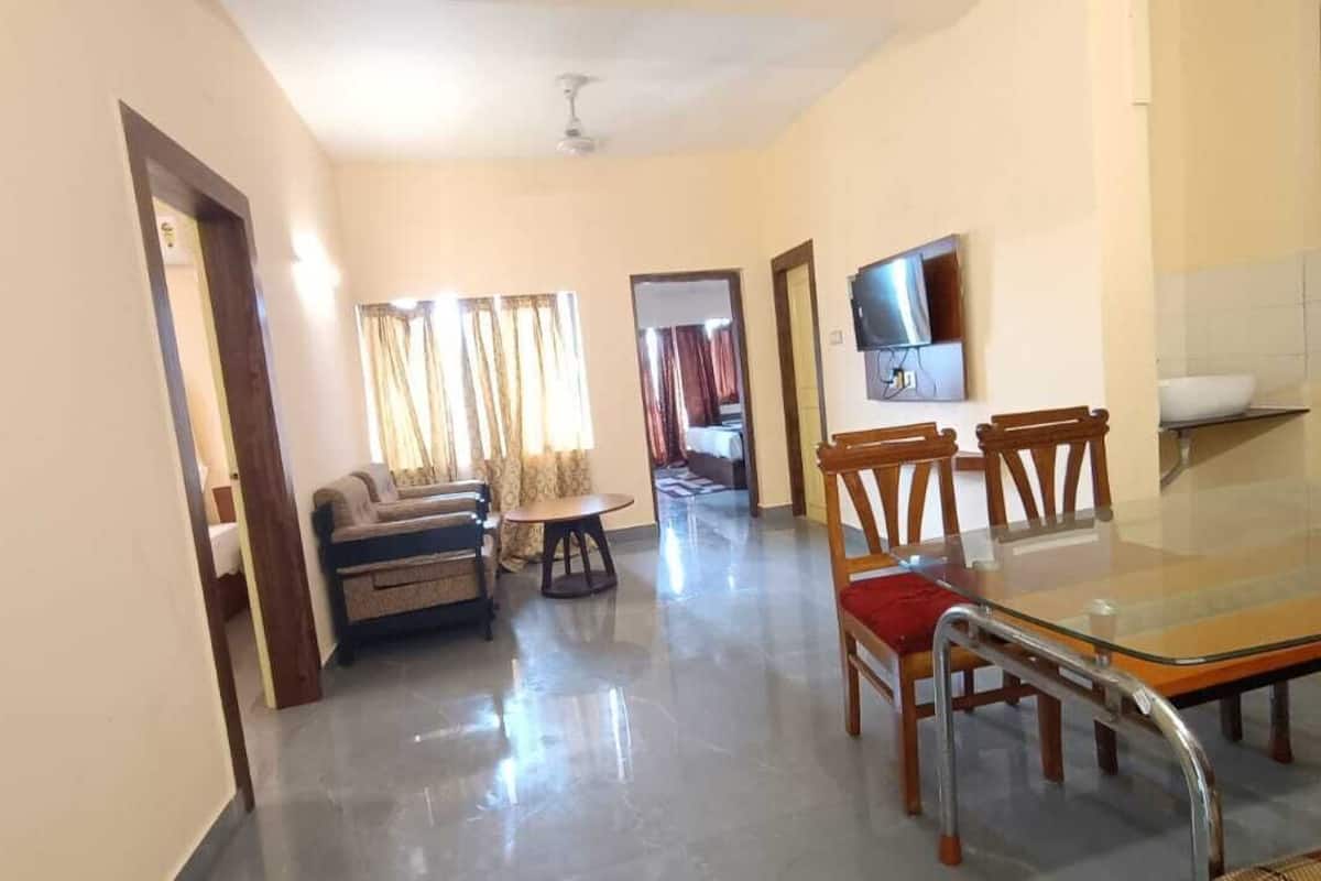 A spacious living room with a sofa, chairs, a glass-top dining table, and a television.