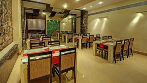 A restaurant with multiple tables and chairs, stone walls, and a green wall in the background. - Hotel Sagar Tarang (Berries Group) (Puri)