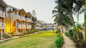 A courtyard with a grassy area, a paved walkway, and a row of multi-story buildings with balconies and air conditioning units. - Hotel Sagar Tarang (Berries Group) (Puri)