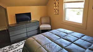 Un dormitorio con una cama, una silla, un tocador, un televisor y una ventana con persianas.