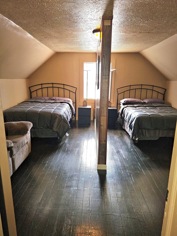 A room with two beds, a wooden floor, and a window.