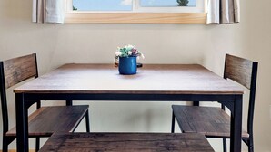 A dining area with a wooden table and benches, a window with curtains, and a potted plant on the table.