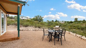 An outdoor patio with a table and chairs, a barbecue grill, and a covered area with a door and windows.