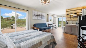 A spacious room with a large bed, a seating area with a sofa, a dining table, and a kitchen area with a refrigerator and sink.
