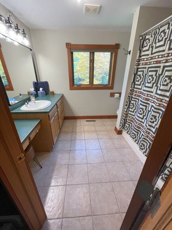 Un baño con lavamanos, espejo, ventana y cortina de ducha estampada.