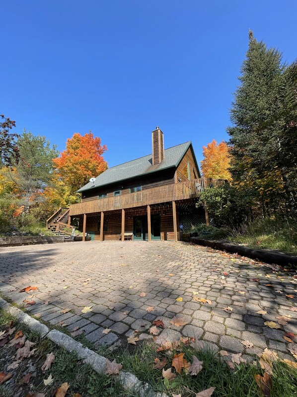 Un chalet rustique doté d’une cour pavée de pierres, d’une terrasse en bois et d’un porche abrité.