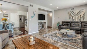 A modern living room with a leather sofa, a coffee table, and a dining area with a chandelier. - Relax at this Family Home w/ Solar heated Pool & Game Room. Close to everything! (San Diego)