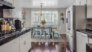 A modern kitchen with stainless steel appliances, a dining area with a chandelier, and a window with sheer curtains. - Relax at this Family Home w/ Solar heated Pool & Game Room. Close to everything! (San Diego)