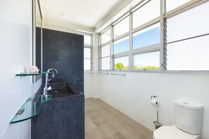 Et moderne badeværelse med en glasbrusekabine, toilet og et vindue med udsigt til grønne omgivelser.