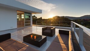 A modern outdoor terrace with a glass balustrade, cushioned seating, and a glass table with drinks. - Secluded Paradise Your Exclusive Villa  (Rawai)