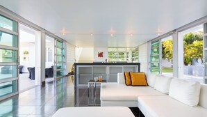 A modern living room with a white sofa, a glass coffee table, and a kitchen area visible through glass doors. - Secluded Paradise Your Exclusive Villa  (Rawai)