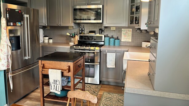 A modern kitchen with grey cabinets, stainless steel appliances, and a wooden island with a 'Hey Y'all' towel.