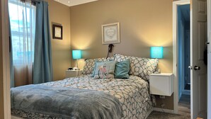A bedroom with a bed, two bedside lamps, a ceiling fan, and a door leading to another room.