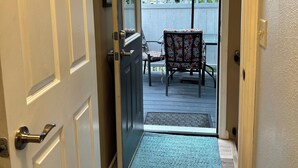 A hallway leading to a patio with a blue umbrella, a chair, and a wooden deck.