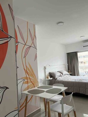 A hotel room with a bed, a small table with chairs, and a decorative panel with abstract leaf patterns.