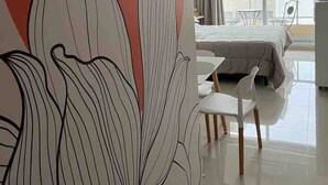 A modern hotel room with a large floral mural, a bed with a grey duvet, a small table with chairs, and a large window offering a view of the city. - Studio In San Telmo La Cisterna Num2689 (Buenos Aires)