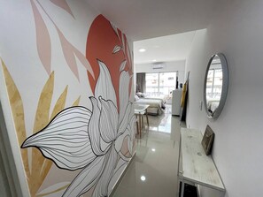 A modern hotel corridor with a large floral mural, a white reception desk, and a large mirror on the wall.